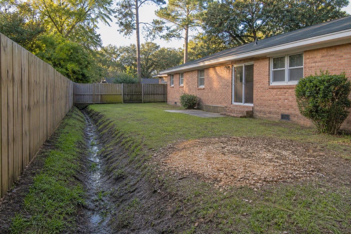 Overgrown drainage ditch line being mulched clear behind backyard fences in a Hanahan neighborhood